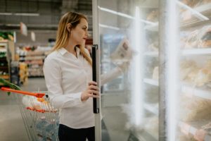 young woman opening a freezer door at the market, reading a product