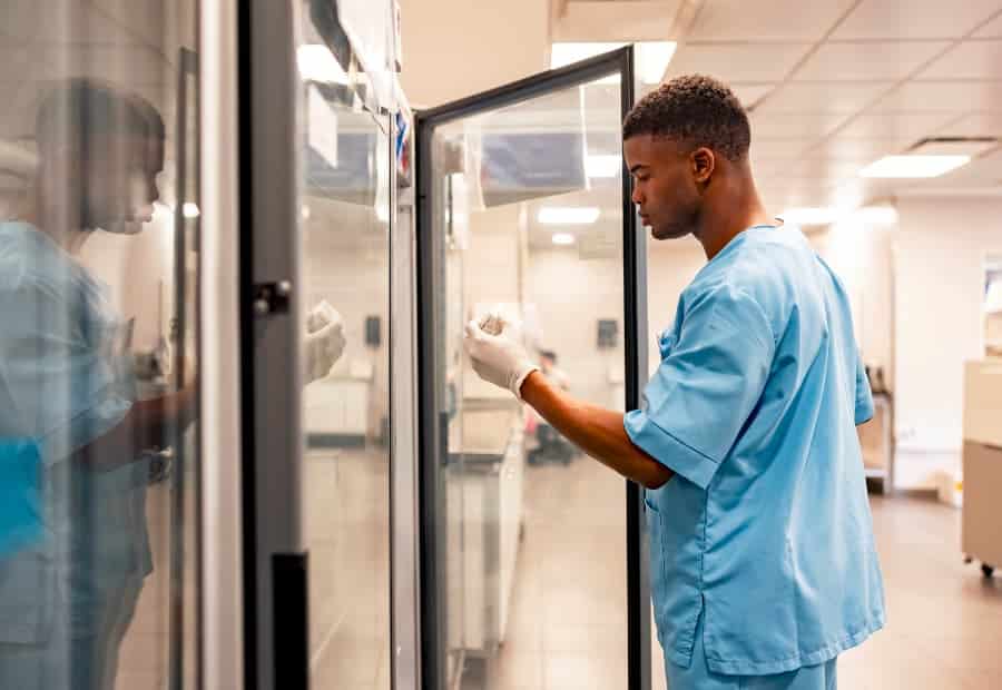 Medical worker in blue scrubs grabbing item from refrigerator